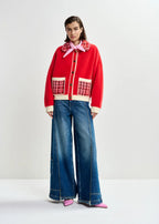 Person wearing a red jacket with plaid accents and blue jeans on a white background