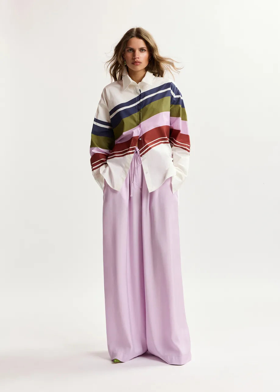 Woman wearing a colorful striped sweater and light purple pants on a white background