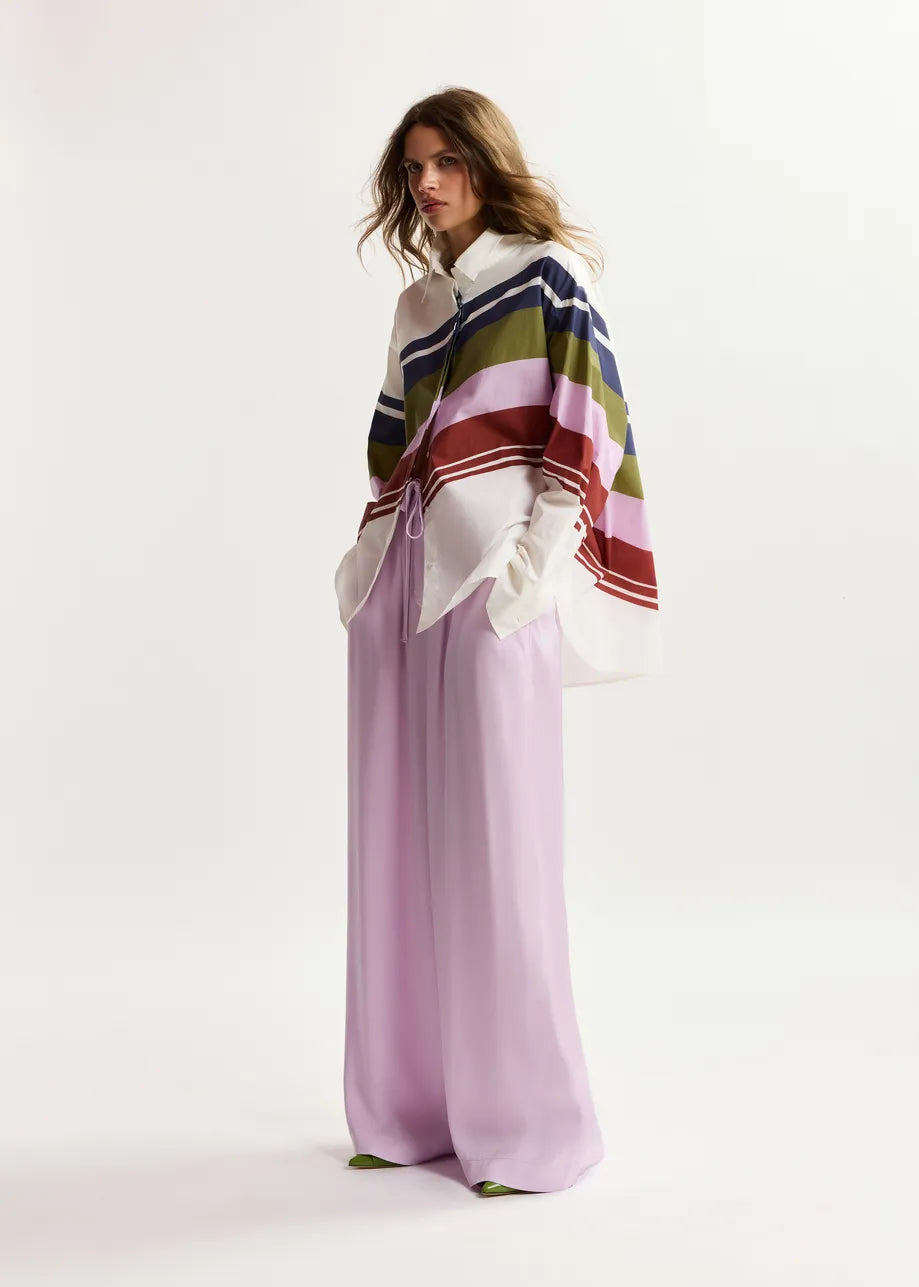 Woman wearing a colorful striped shawl over a white top and light purple pants on a white background