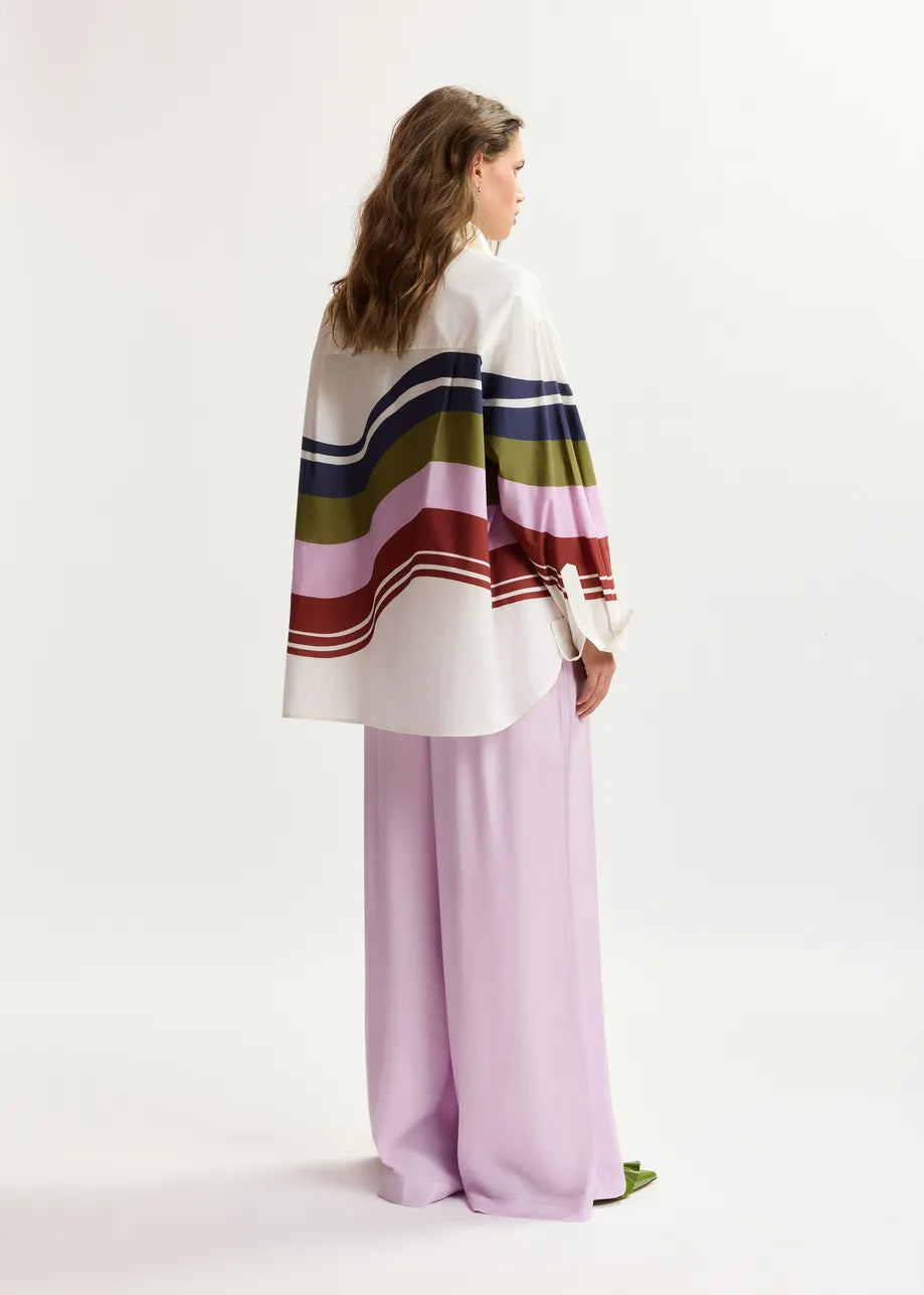 Woman wearing a colorful striped poncho and light purple pants on a white background