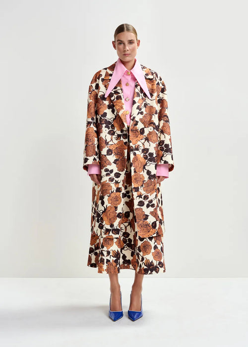 Model wearing a patterned coat with a pink shirt underneath on a white background