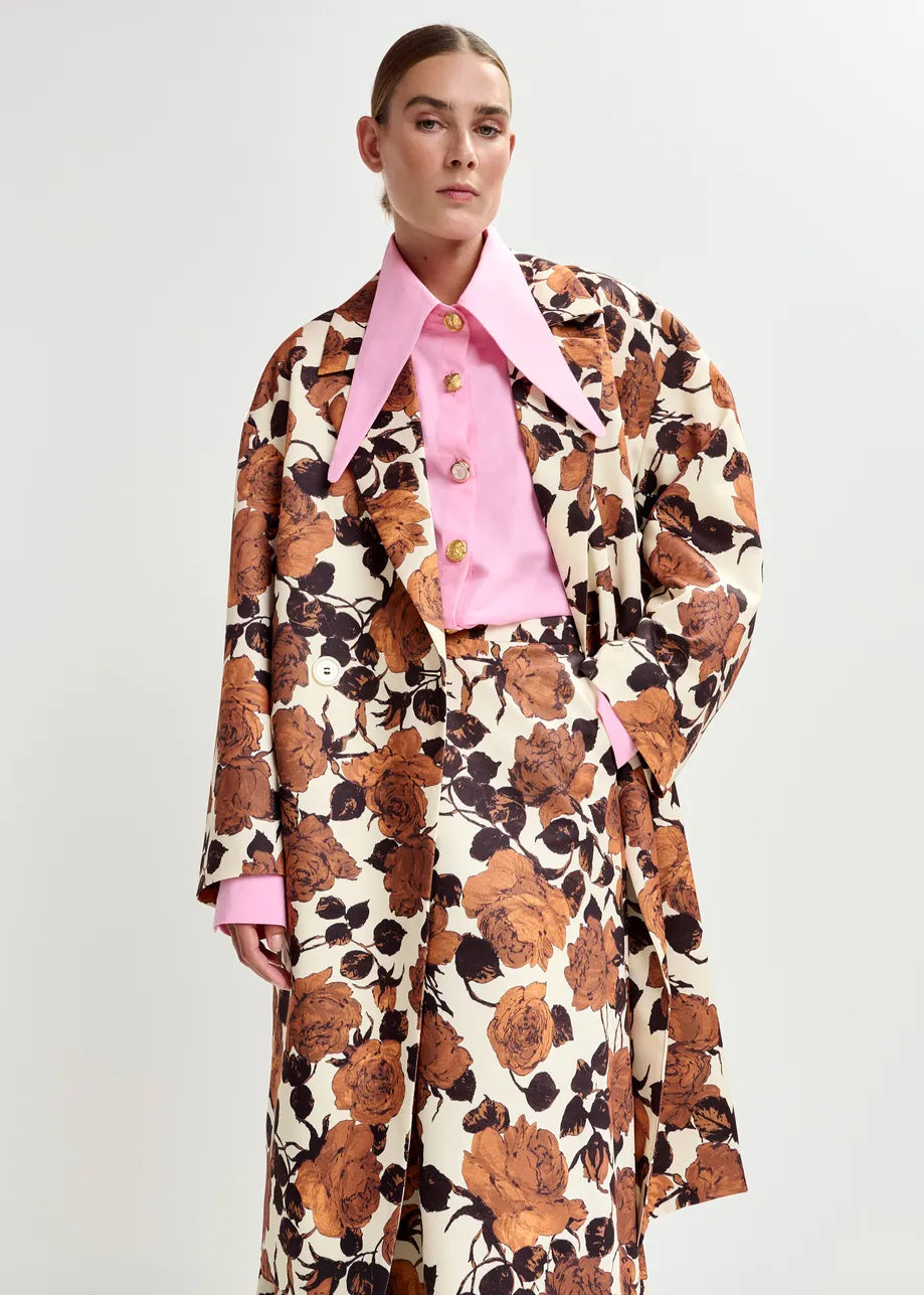 Model wearing a floral coat over a pink shirt on a white background
