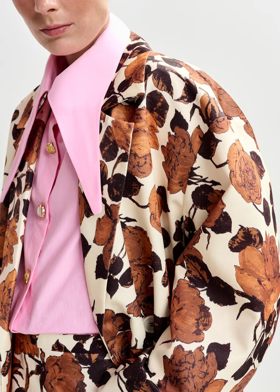 Person wearing a floral patterned coat over a pink shirt on a plain background