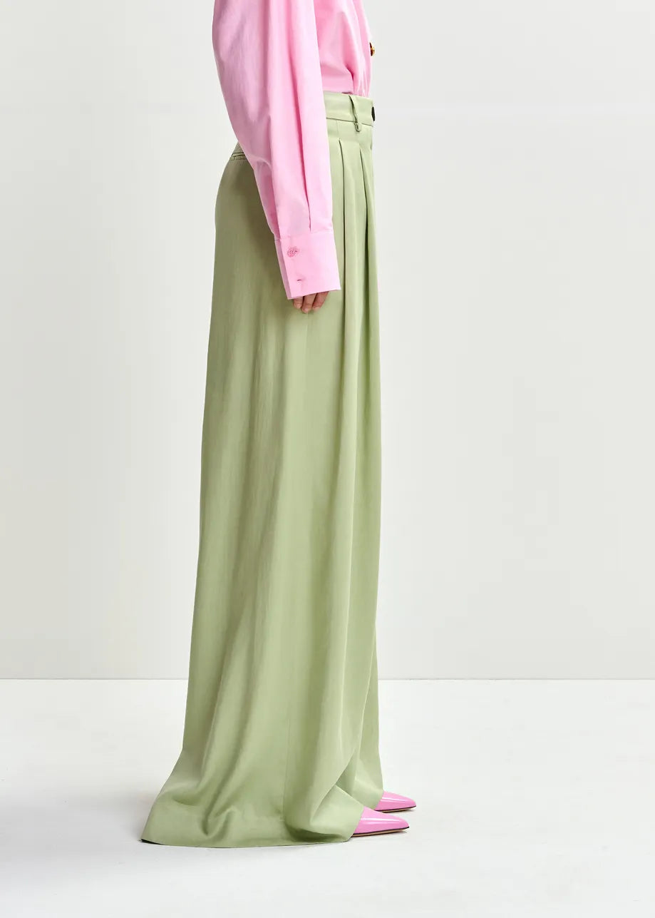 Person wearing a pink top and green wide-leg pants on a white background
