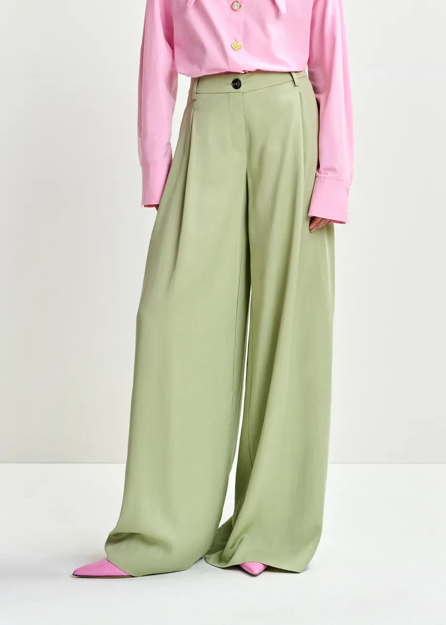 Person wearing a pink shirt and green wide-leg pants on a white background