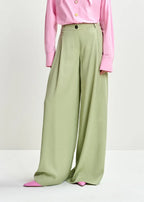Person wearing a pink shirt and green wide-leg pants on a white background