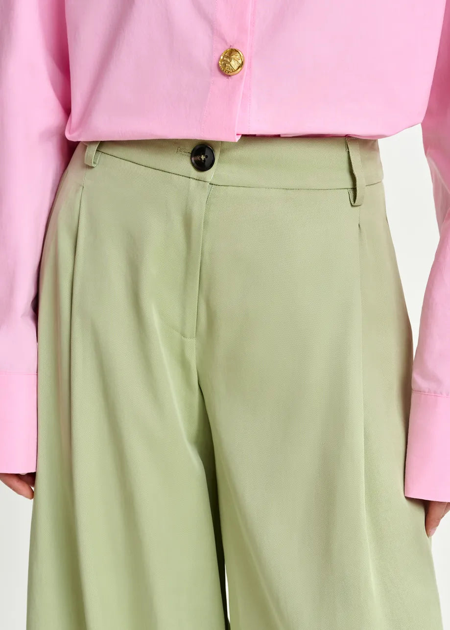 Person wearing a pink shirt and light green pants with a gold button.