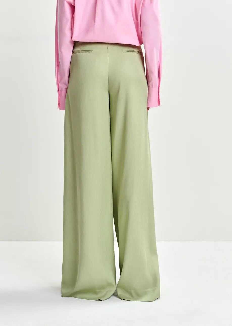 Green wide-leg pants worn with a pink top on a white background