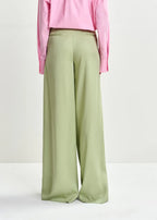 Green wide-leg pants worn with a pink top on a white background
