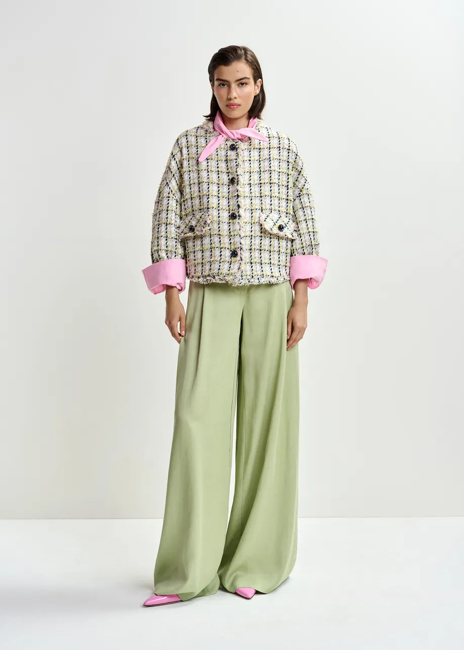 Woman wearing a patterned jacket with pink cuffs and collar, paired with wide-leg green pants on a white background.