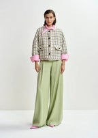 Woman wearing a patterned jacket with pink cuffs and collar, paired with wide-leg green pants on a white background.