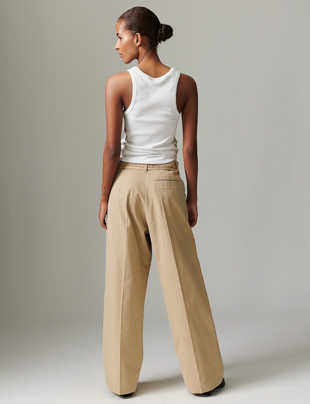 Woman wearing a white tank top and beige wide-leg pants against a plain background