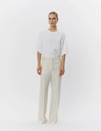 Person wearing a white oversized shirt and beige pants on a white background