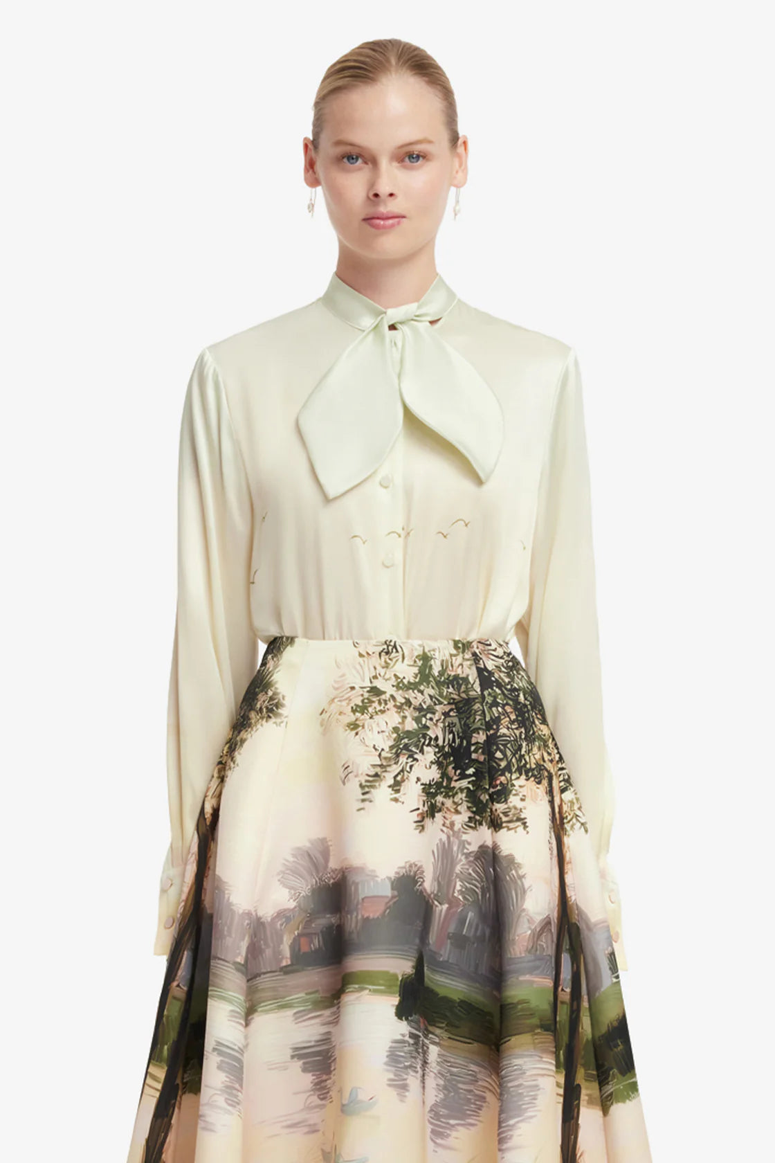 Woman wearing a light-colored blouse with a tie collar and a scenic skirt on a white background