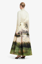 Woman wearing a long, light-colored dress with a scenic print on a white background