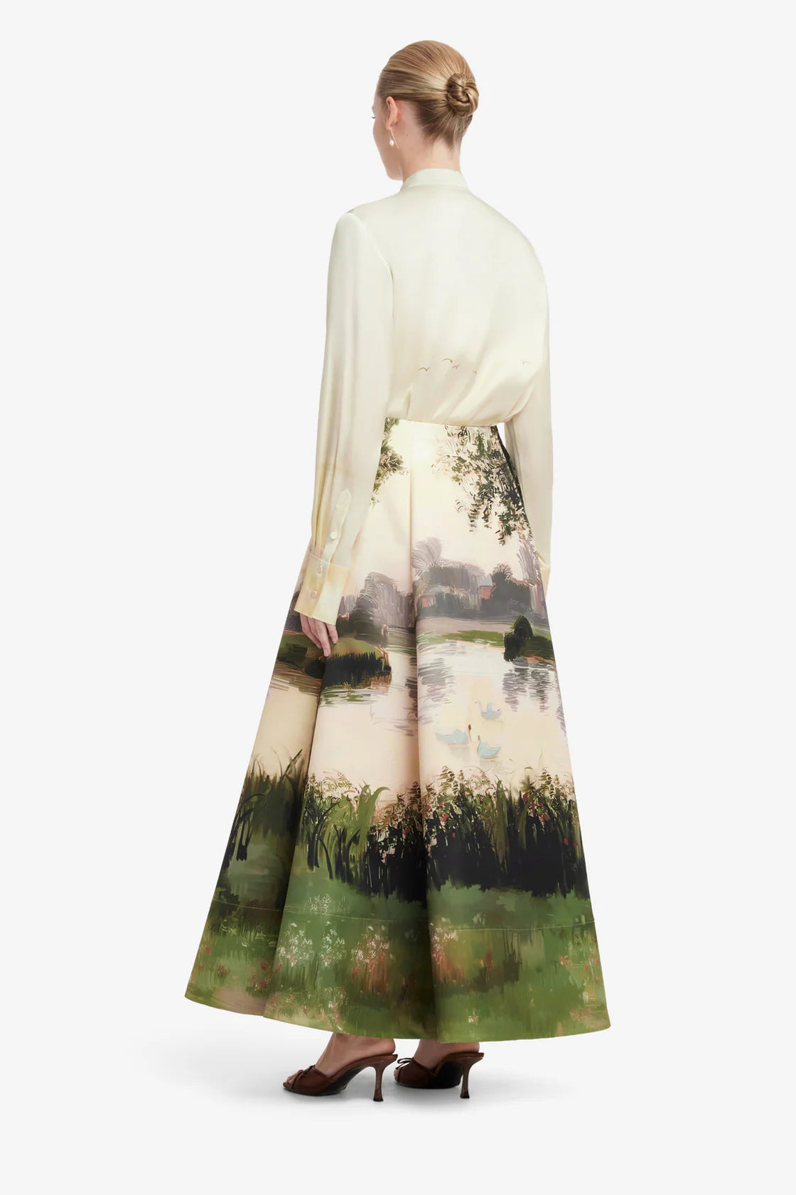 Woman wearing a long, light-colored dress with a scenic print on a white background