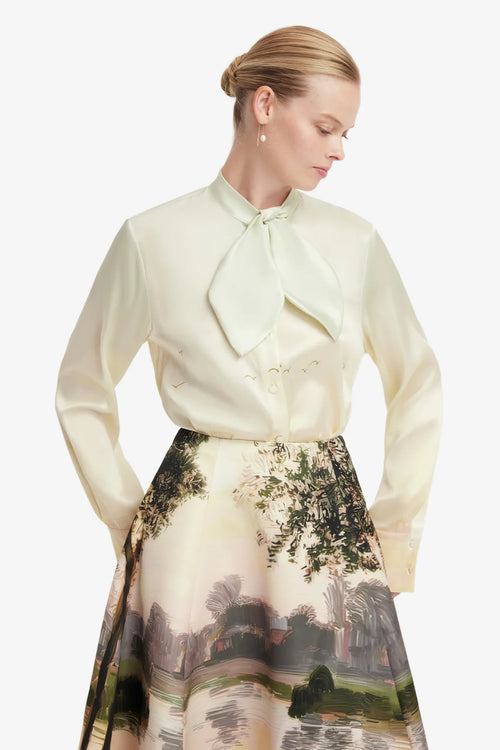 Woman wearing a light-colored blouse with a bow tie and a scenic skirt on a white background