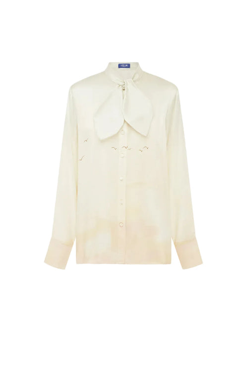 A cream-colored long-sleeve button-up shirt with a large bow tie collar and subtle embroidered bird motifs, displayed on a clean white background.