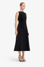 Woman wearing a black sleeveless dress with bow details on a white background