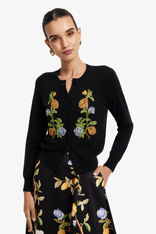 Woman wearing a black embroidered cardigan and skirt with floral patterns on a white background