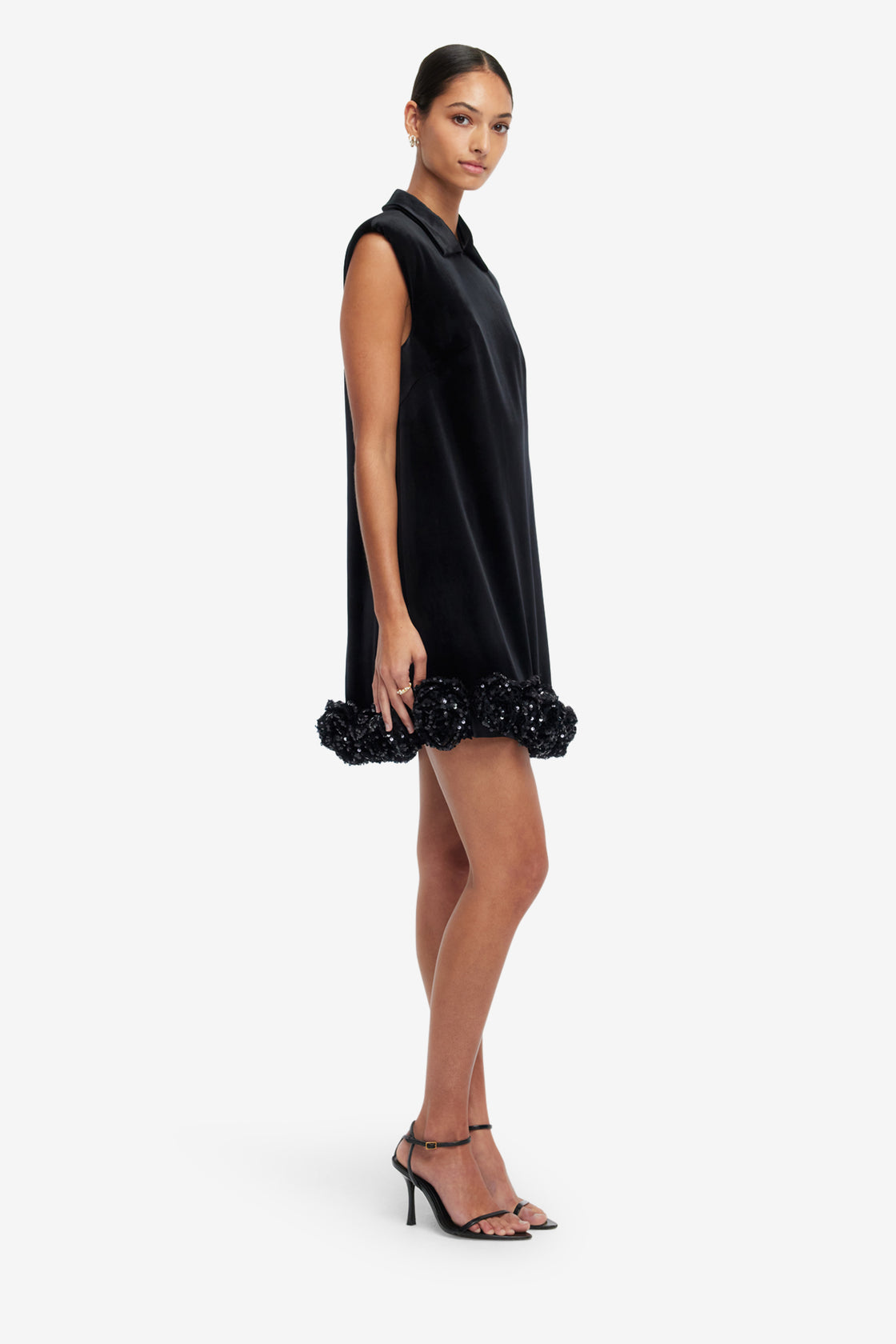 Woman wearing a black sleeveless dress with floral details on a white background