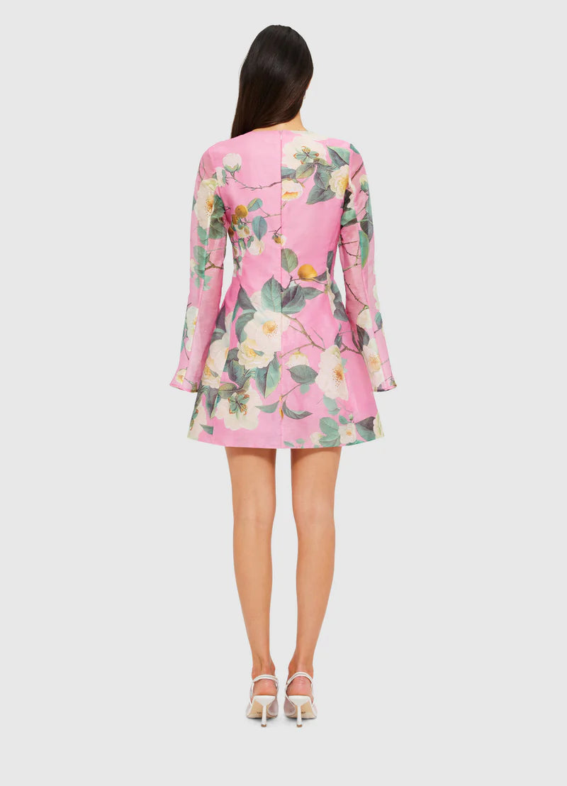 A model standing against a white background wearing a pink floral dress with long sleeves and a knee-length hem.