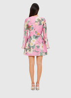 A model standing against a white background wearing a pink floral dress with long sleeves and a knee-length hem.