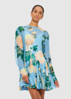 A woman wearing a floral Mia Mini Dress in Cornflower Blue, standing against a white background.