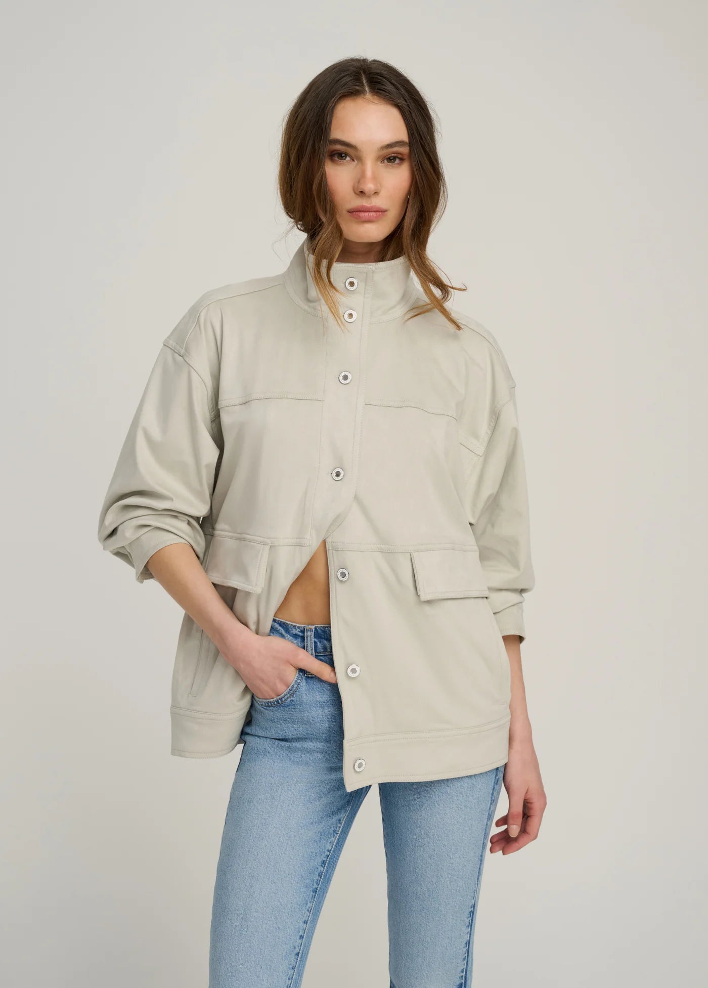 Woman wearing a beige jacket and blue jeans on a plain background