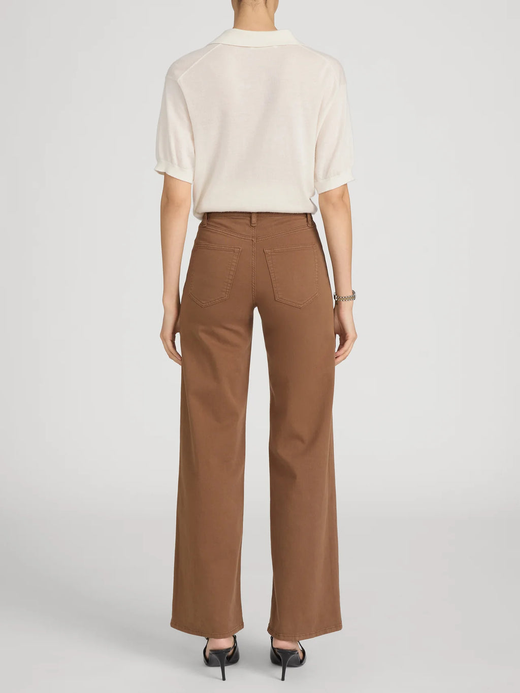 Person wearing a white shirt and brown pants on a light gray background