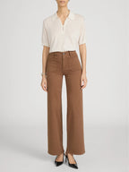 Person wearing a white blouse and brown pants on a plain background