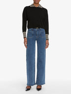 Person wearing a black sweater with white stripes and blue jeans on a white background