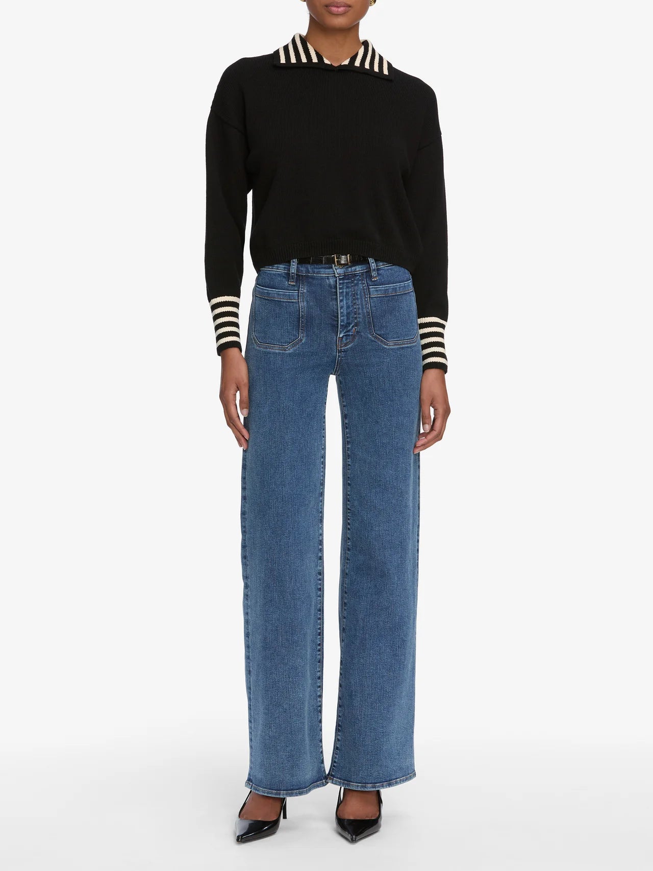 Person wearing a black sweater with white stripes and blue jeans on a white background