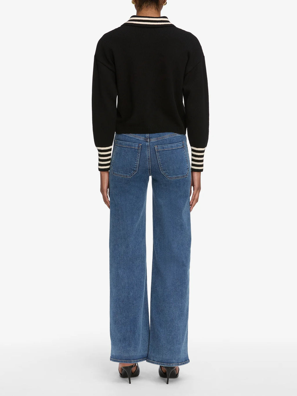 Person wearing a black sweater with striped cuffs and blue jeans on a white background
