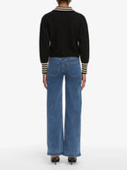 Person wearing a black sweater with striped cuffs and blue jeans on a white background