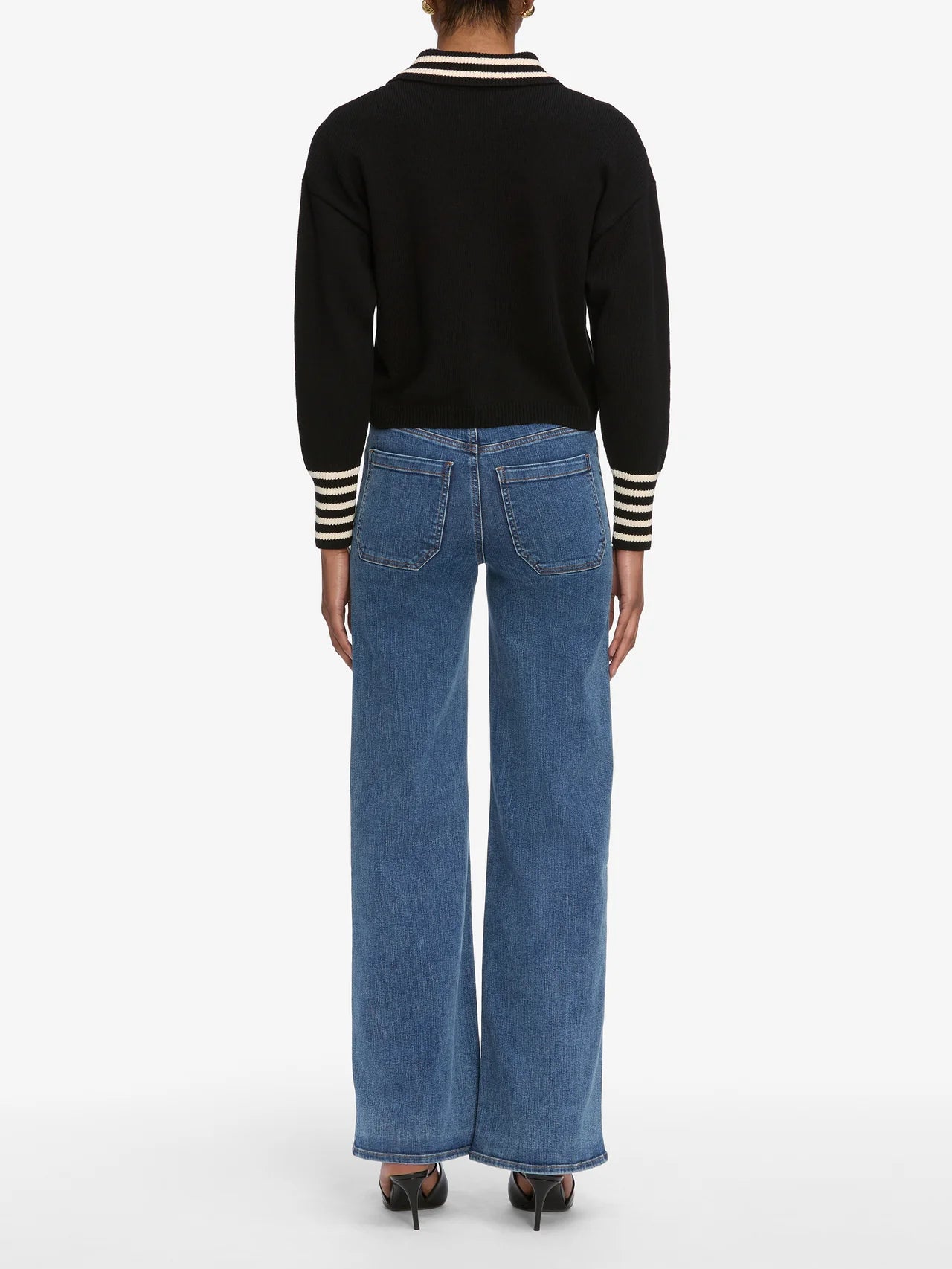 Person wearing a black sweater with striped cuffs and blue jeans on a white background