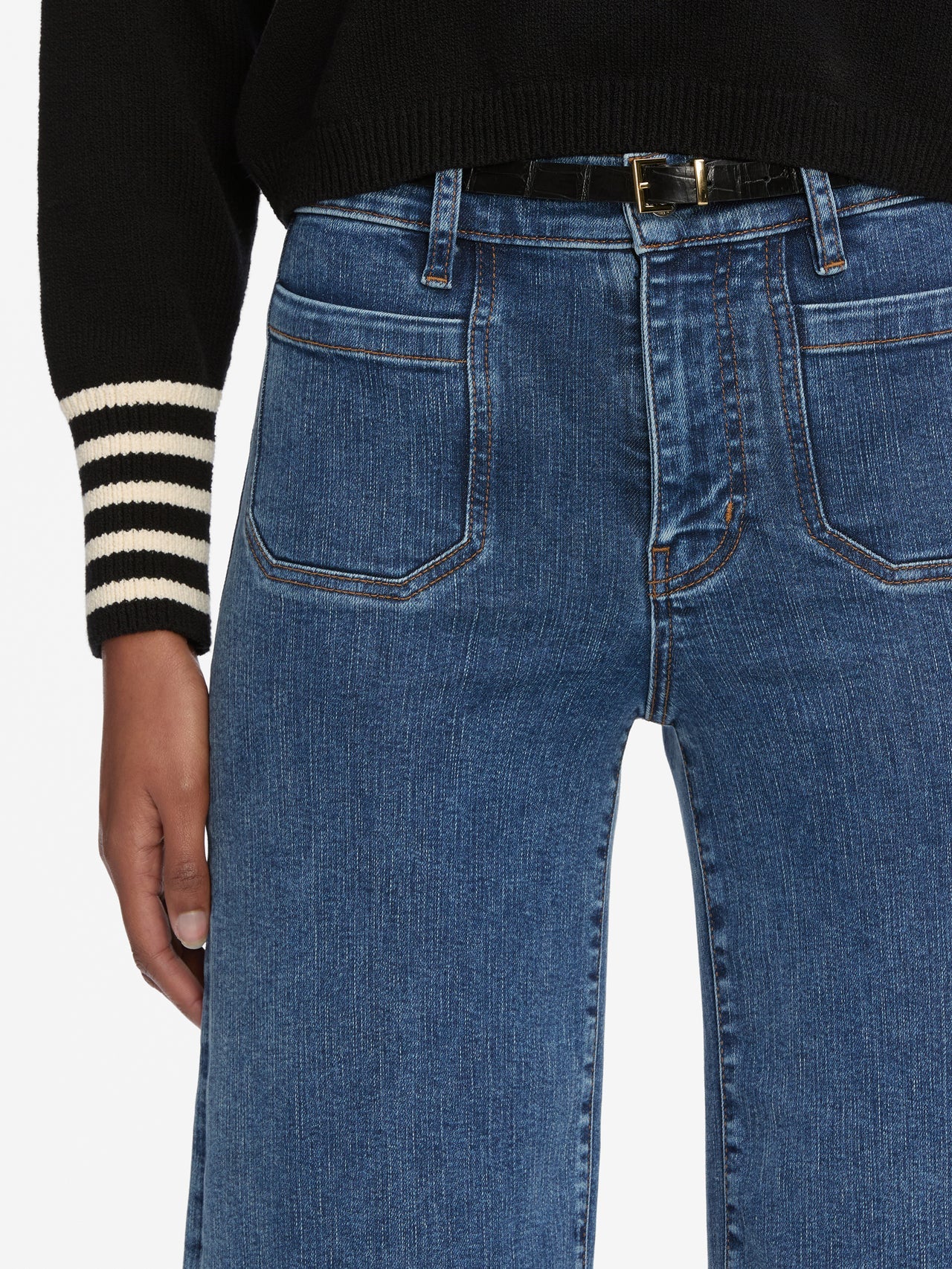 Blue jeans worn with a black sweater and striped sleeve on a white background