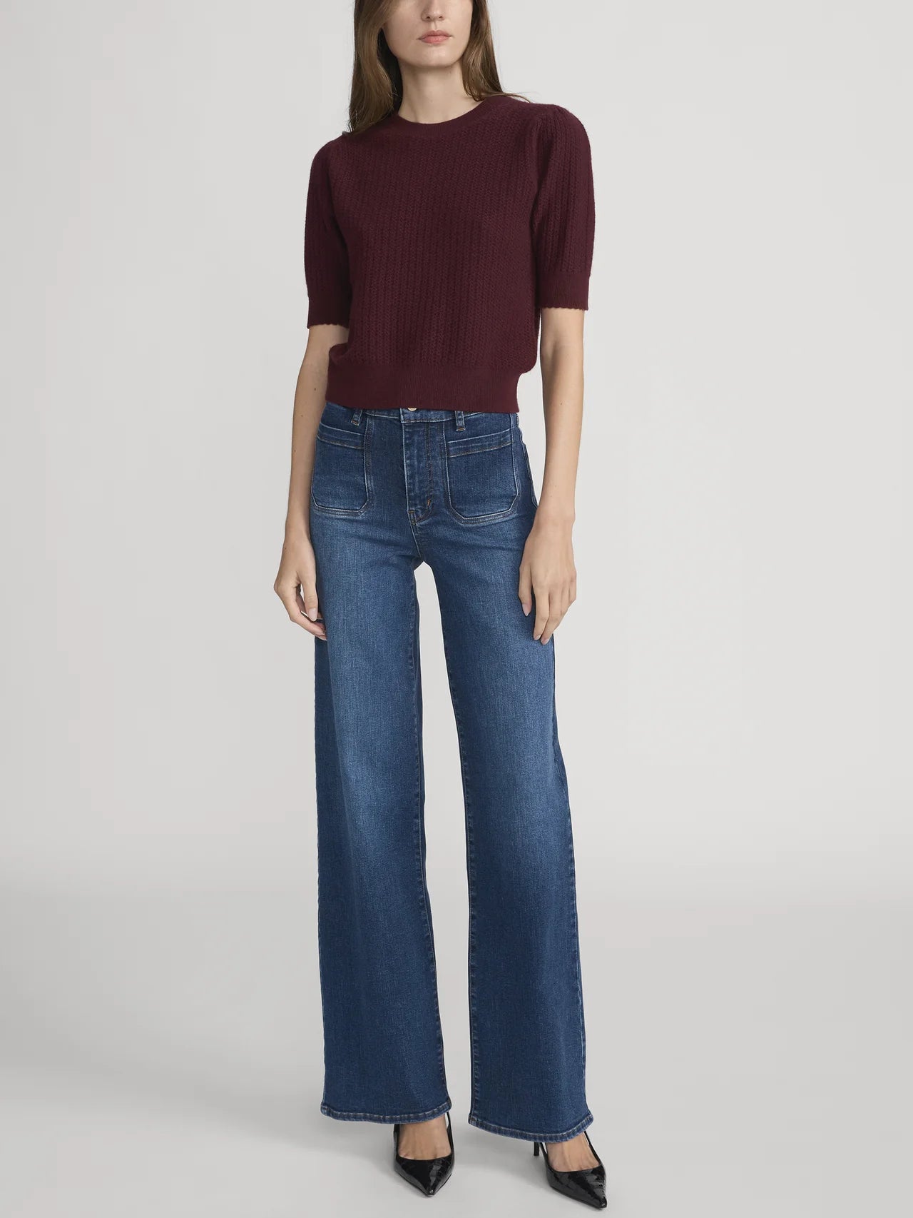 Person wearing a burgundy sweater and blue jeans on a white background