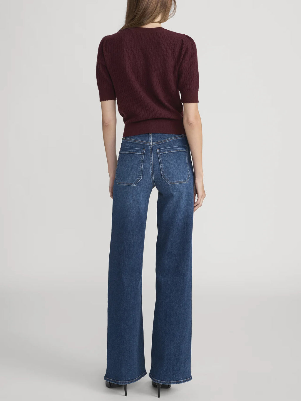 Person wearing a burgundy top and blue jeans on a light gray background