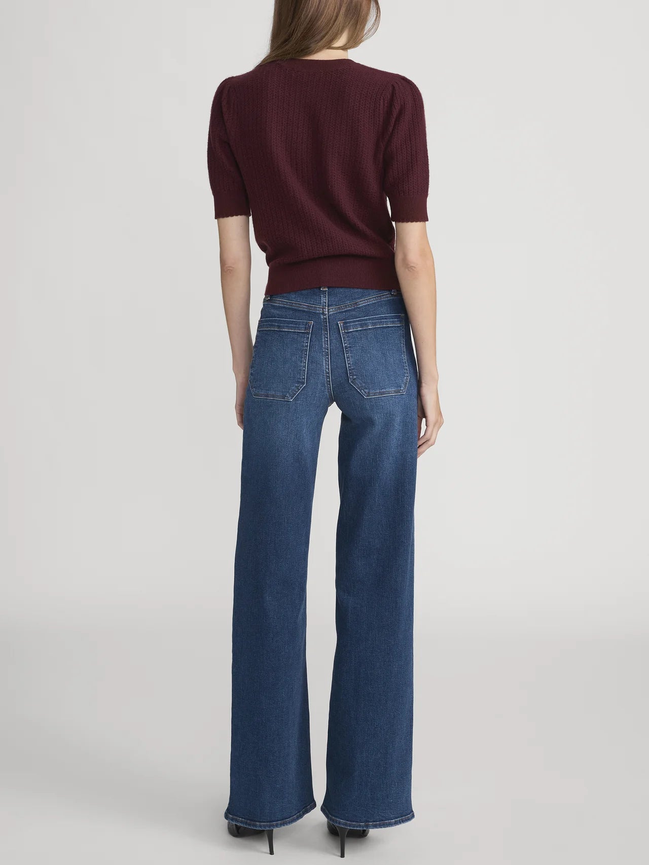 Person wearing a burgundy top and blue jeans on a light gray background