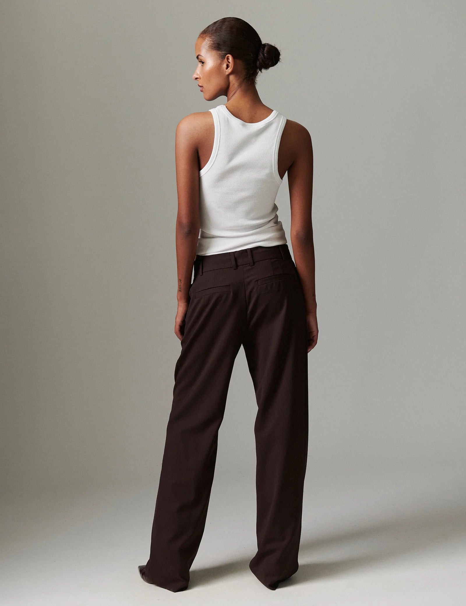 Woman wearing a white sleeveless top and brown pants against a plain background