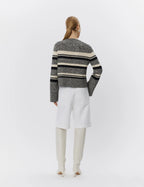 Person wearing a striped sweater and white pants on a light gray background