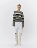 Person wearing a striped sweater and white pants with knee-high boots on a white background
