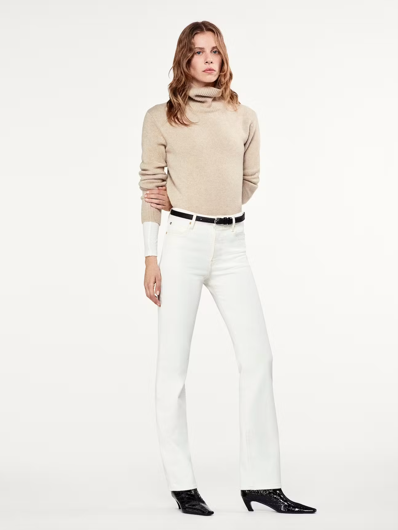 A model wearing high-rise straight leg jeans and a beige turtleneck sweater with a black belt.