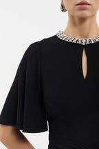 A close-up of a model wearing a black short-sleeve dress with a keyhole neckline and a wide collar embellished with sparkling rhinestones.