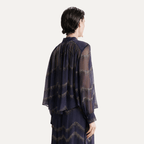 A model shown from the back wearing a dark navy sheer long-sleeve blouse with a subtle wavy metallic pattern, paired with a matching navy skirt, against a light gray studio background.