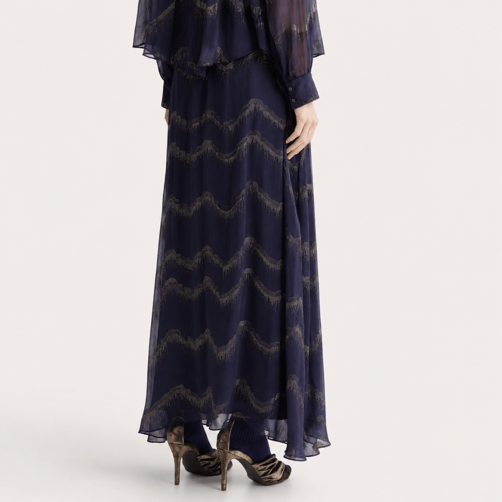 A navy blue maxi dress with a metallic gold wavy pattern, shown on a model from the back against a light gray studio background.