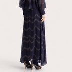 A navy blue maxi dress with a metallic gold wavy pattern, shown on a model from the back against a light gray studio background.