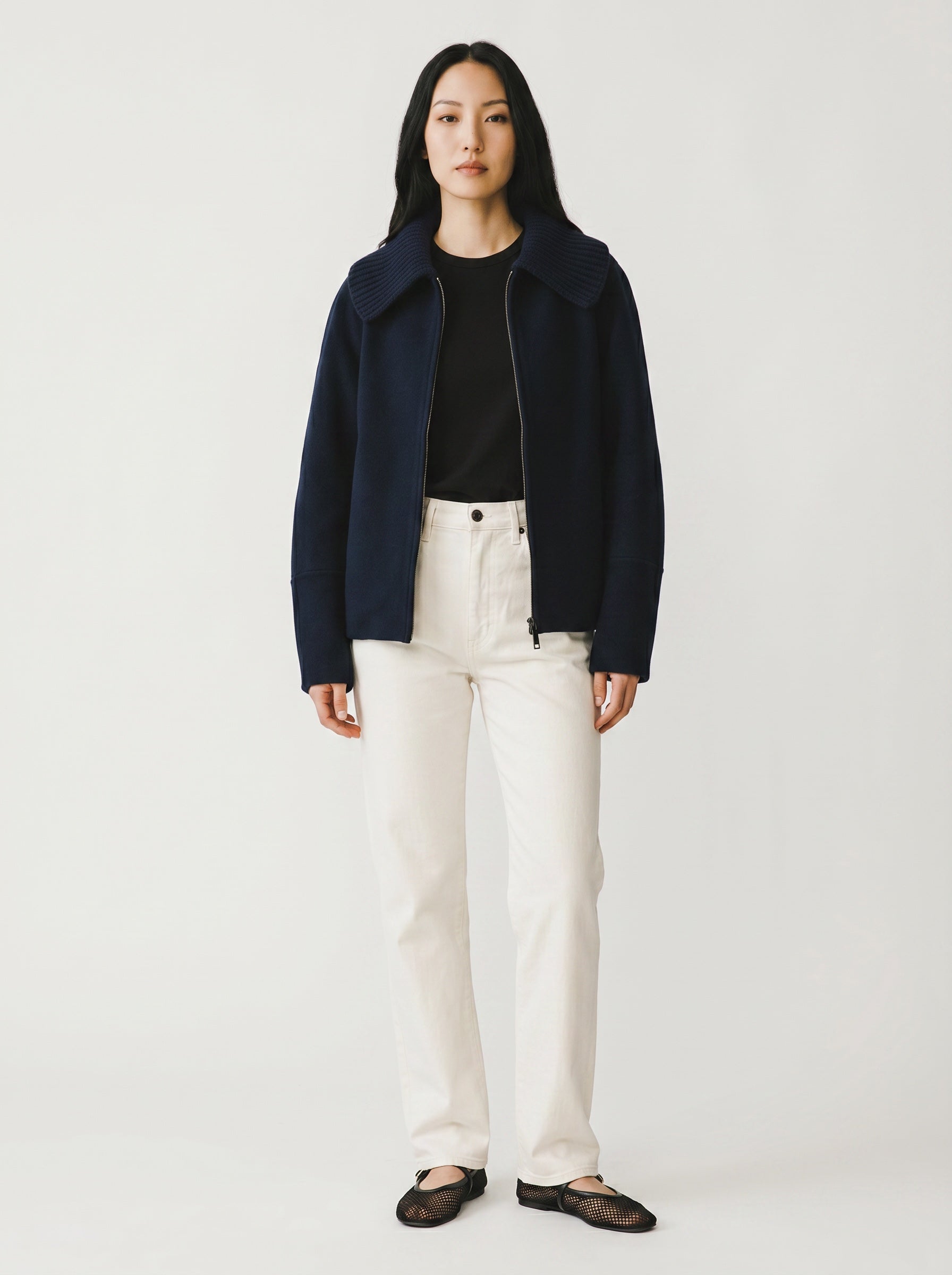 Person wearing a navy coat, black top, and white pants on a plain background