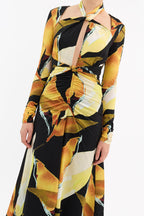 A long sleeve midi dress with a vibrant golden printed design, featuring a tied neckline and a knotted waist.